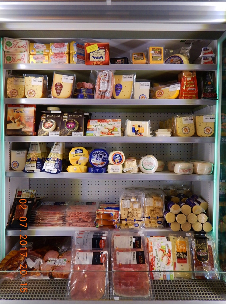 A geladeira onde a clientela encontra variados tipos de queijos e frios. A mercearia oferece marcas variadas dos mesmos produtos.